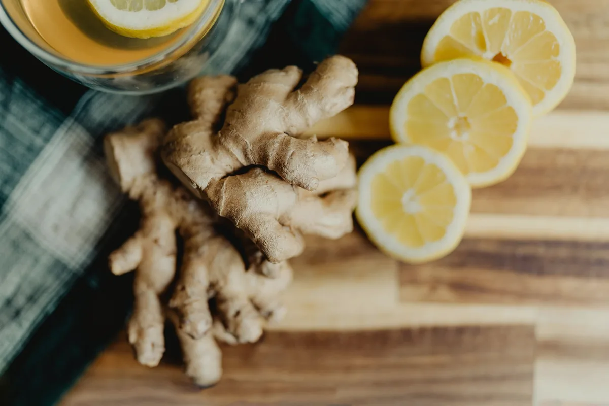 Rhizomes de gingembre et rondelles de citron sur une planche, avec une tasse d'infusion