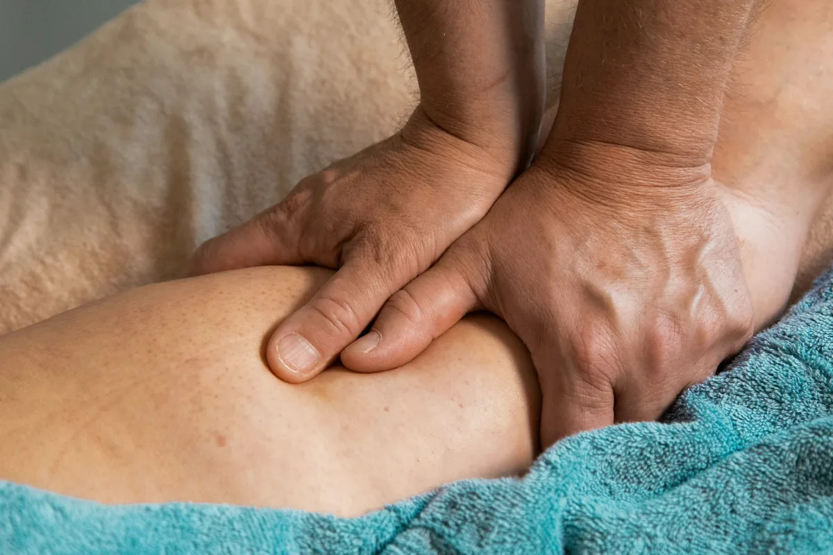 Deux mains posées sur un avant-bras recouvert d'une serviette turquoise, pendant un massage
